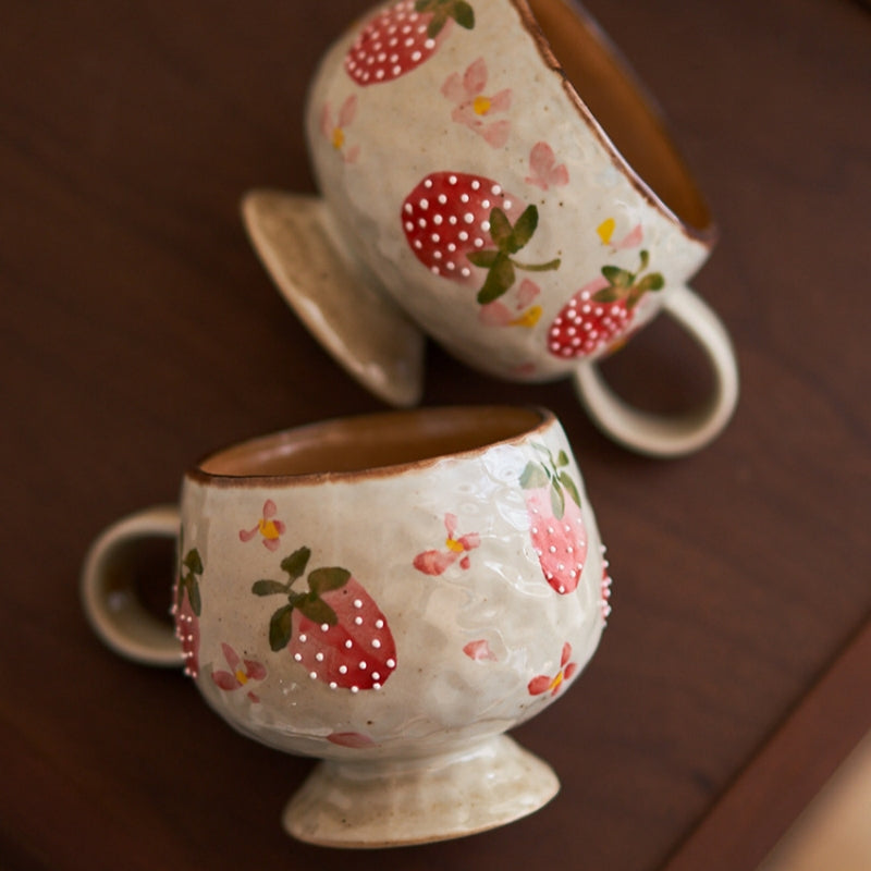 Two Ceravor strawberry ceramic mugs on a dark wooden table