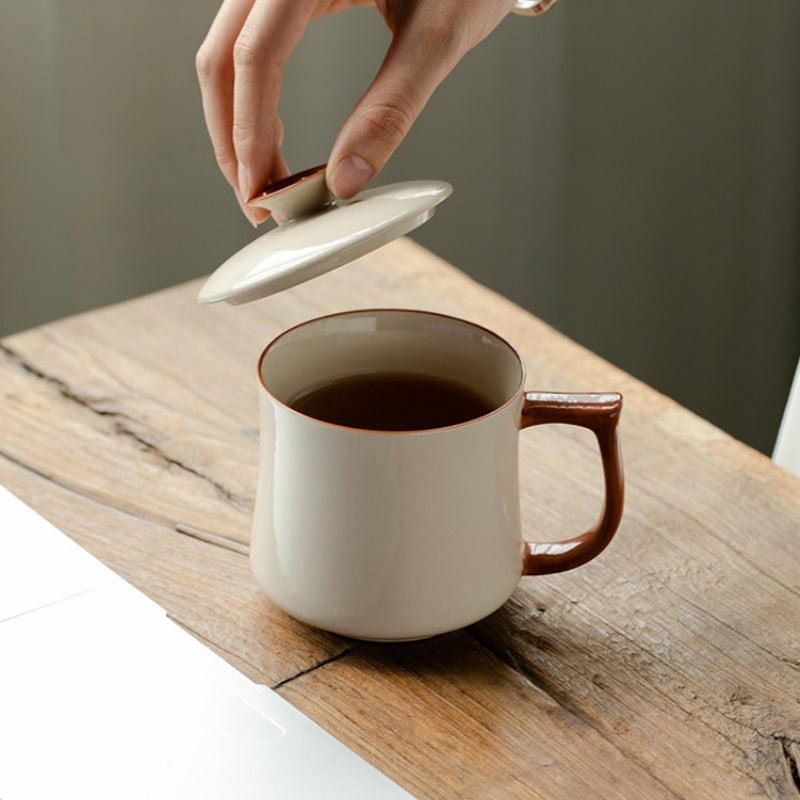 Person lifting the lid off a Ceravor ceramic mug with tea on a wooden desk
